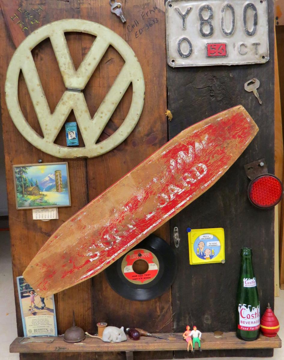 A license plate, small surf board, VW logo, picture of water and an old record on a wooden wall.