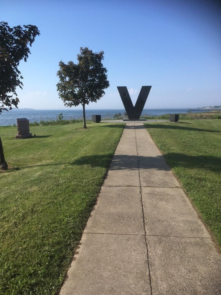 Large metal V at end of walkway with grass on both sides.