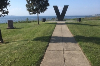 Large metal V at end of walkway with grass on both sides.